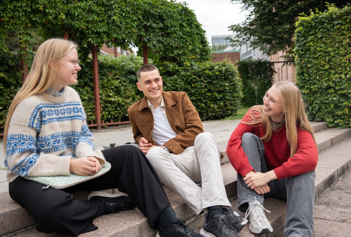 Tre studenter sittende på en trapp ute