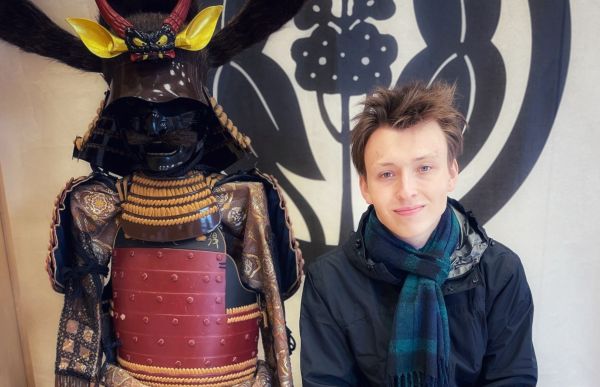 n ung mann sitter ved siden av en tradisjonell japansk samuraidraktsfigur.