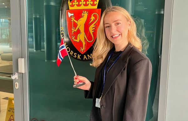 Kvinne med langt blondt hår. Hun har svart dressjakke og dressbukse. Hun smiler.